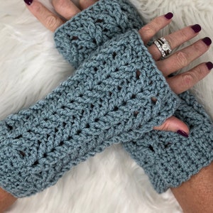 May include: A pair of blue crocheted fingerless gloves with a lacy pattern. The gloves are worn on a person's hands.