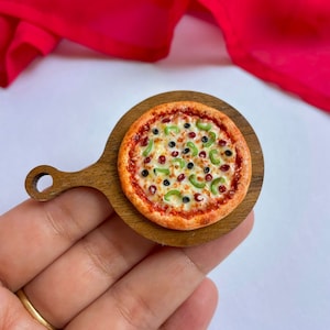 Peut inclure: Une mini pizza avec des poivrons verts, des olives noires et des flocons de piment rouge sur une petite planche à découper en bois.