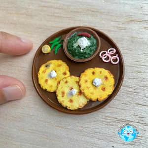 Könnte beinhalten: Miniatur-Braunteller mit drei gelben Fladenbroten, einer Schüssel mit grünem Essen mit weißem Belag und grünen Paprika. Der Teller hat auch eine Zitronenscheibe und rosa Zwiebelringe. Das Essen ist auf einer hellbraunen Oberfläche angeordnet.