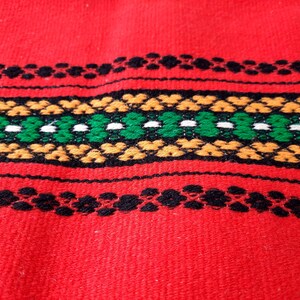 Pu&ograve; includere: Tessuto rosso tessuto con un motivo geometrico nero, verde, bianco e arancione.