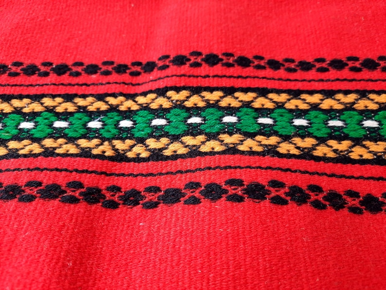 Pu&ograve; includere: Tessuto rosso tessuto con un motivo geometrico nero, verde, bianco e arancione.