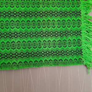 May include: Green and black woven throw blanket with fringe on the edges.