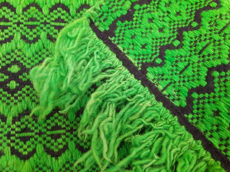 May include: Close-up of a green and black woven rug with a fringe border. The rug has a geometric pattern.
