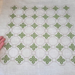 Puede incluir: Un mantel de lino blanco con un patrón bordado verde de formas geométricas repetidas.