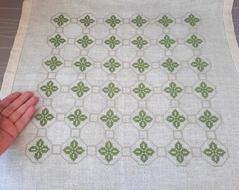 Può includere: Un tovaglia di lino bianco con un motivo ricamato verde di forme geometriche ripetute.