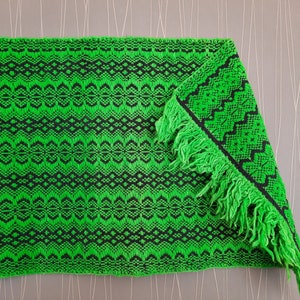 May include: A green and black woven rug with fringe. The rug has a geometric pattern.