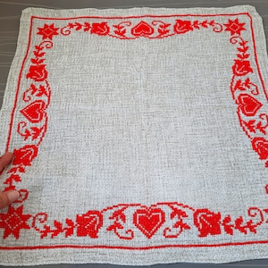 Puede incluir: Un mantel individual de lino blanco con un borde bordado en rojo que presenta corazones, hojas y estrellas.