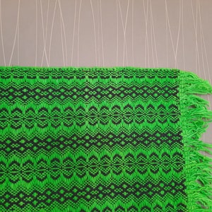May include: Green and black woven rug with fringe on the edges. The rug has a geometric pattern.