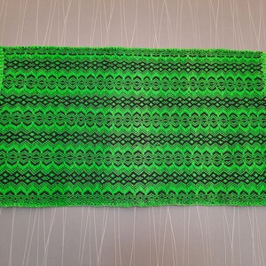 May include: A green and black woven rug with fringe on all sides. The rug has a geometric pattern.