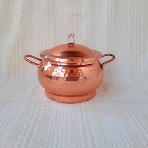 May include: A hammered copper pot with a lid and two handles. The pot is a traditional design and has a shiny finish.