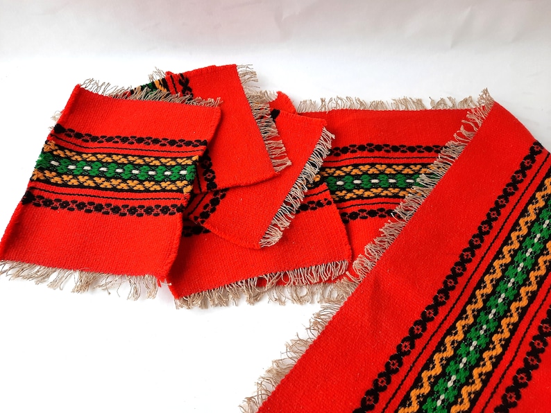Pu&ograve; includere: Set di tovagliette all'americana in tessuto rosso con motivi geometrici neri, verdi e arancioni e bordi a frangia.