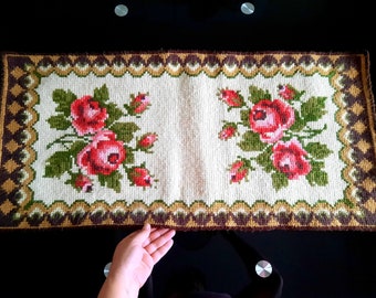 Può includere: Un tappeto rettangolare color crema con un bordo marrone e dorato. Il tappeto è ricamato con rose rosse e verdi.