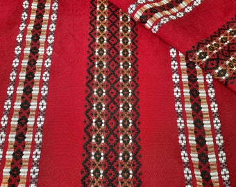 Può includere: Tessuto rosso con intricati motivi tessuti. Il design presenta strisce verticali con motivi geometrici e floreali in bianco, nero e marrone. Il tessuto è piegato, mostrando la lavorazione artigianale.