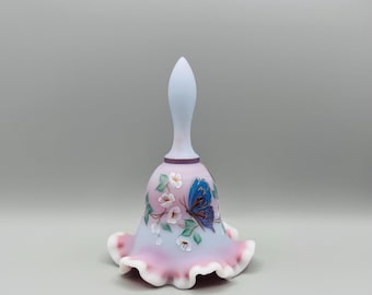 Puede incluir: Una campana decorativa con un asa azul claro y una base acampanada y con volantes. La campana presenta un degradado rosa y azul claro con un diseño de mariposa y flores pintadas. La campana es un objeto de colección.