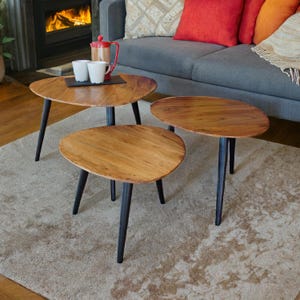 May include: Three wooden nesting tables with black metal legs. The tables are shaped like irregular ovals and are arranged in a staggered formation on a beige rug.