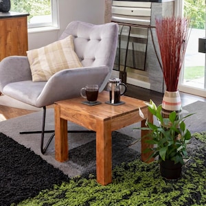 May include: A light grey armchair with a beige patterned cushion sits next to a wooden end table with two coffee cups and a French press. A green plant in a black pot sits on the rug next to the table.
