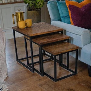 May include: A set of three nesting tables with dark wood tops and black metal frames. The tables are arranged in descending size, with the largest table at the top. The wood tops have a carved design. The tables are 61 cm, 51 cm, and 41 cm wide.
