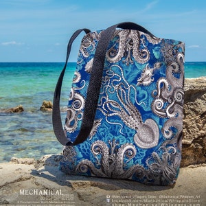 May include: A blue tote bag with a white and gray octopus design. The bag has black straps and is sitting on a rocky surface near the ocean.
