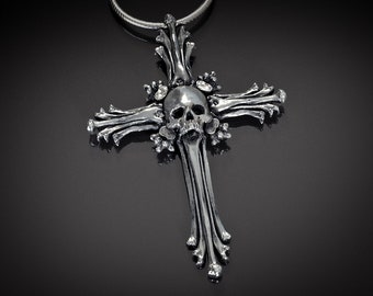 Könnte beinhalten: Eine silberne Totenkopf-Halskette mit einem Kreuzdesign. Das Kreuz besteht aus knochenartigen Details und hat kleine Strasssteine.