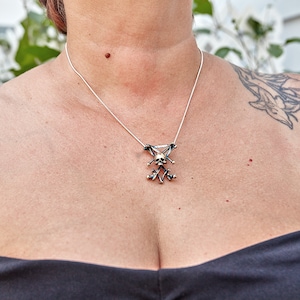 K&ouml;nnte beinhalten: Eine silberne Kettenkette mit einem Anh&auml;nger mit Totenkopf- und Knochenkreuz-Motiv. Der Anh&auml;nger ist aus Metall mit goldener Oberfl&auml;che und hat einen detaillierten Totenkopf mit gekreuzten Knochen.
