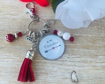 May include: A silver keychain with a red tassel, a silver charm that says "Love", and a round charm that says "Be My Valentine" with a red heart and arrow.