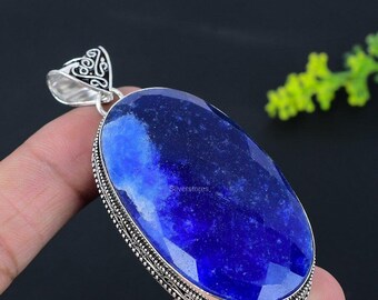 Op de afbeelding: Een ovaalvormige hanger met een grote, gefacetteerde diepblauwe lapis lazuli edelsteen, gezet in een decoratieve sterling zilveren rand met ingewikkelde metaalpatronen en een bijpassende versierde zilveren hangerlus aan de bovenzijde.