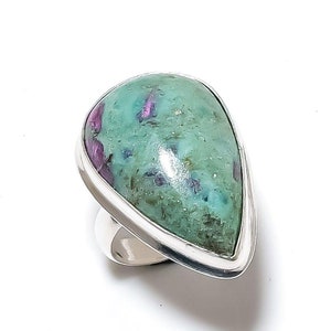 May include: A silver ring featuring a large, teardrop-shaped gemstone. The stone is a mix of teal and green with flecks of deep red. The ring has a polished silver band and bezel setting, creating a striking contrast with the colorful stone.