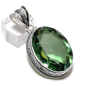 May include: A silver pendant featuring an oval green gemstone. The pendant has an elaborate silver design surrounding the gemstone.