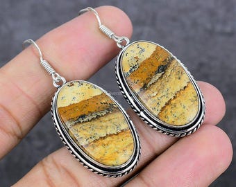 May include: A pair of oval-shaped earrings with a silver-colored frame. The earrings feature a natural stone with a pattern of tan, brown, and cream colors. The earrings have a hook closure.