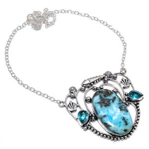May include: A silver necklace with a large blue and white gemstone pendant. The pendant is surrounded by smaller blue gemstones and intricate silver detailing.