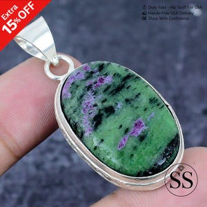 Puede incluir: Colgante ovalado de plata con una piedra verde y morada. La piedra presenta un patrón distintivo con inclusiones negras. El colgante está engastado en un bisel de plata y tiene una fianza de plata. El texto "Extra 15% OFF" también es visible.