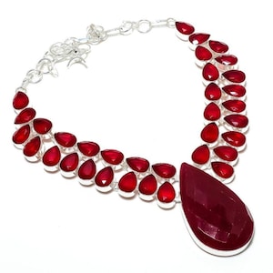 Peut inclure: Un collier en argent avec un grand pendentif en pierre rouge et de plus petites pierres rouges disposées en forme de goutte d'eau autour du pendentif.