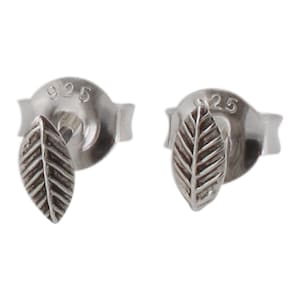 May include: A pair of silver earrings with a small leaf design. The earrings are marked "925" on the back.