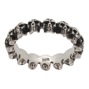 May include: A silver ring with a band of skulls. The skulls are all facing the same direction and are arranged in a circle around the band.