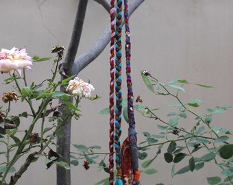 May include: A colorful braided cord with multiple bells hanging from it. The cord is made of different fabrics and colors, including red, pink, blue, and green. The bells are silver and have a conical shape.