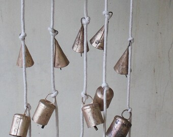 May include: A string of small, gold-colored bells hanging from white cords. The bells are of various shapes, including round, cone-shaped, and bell-shaped. The bells are arranged in a cascading pattern, with the longest cords at the top and the shortest cords at the bottom.