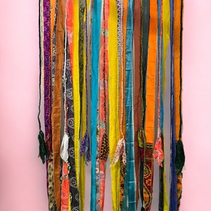 Op de afbeelding: Een kleurrijk gordijn van stof gemaakt van stroken stof in verschillende kleuren en patronen, waaronder geel, oranje, blauw, groen en paars.