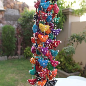 May include: A vibrant beaded garland with fabric bird decorations in diverse colours, such as red, blue, yellow, and green. The birds are decorated with white polka dots and hang from a string with small bells at the base. A decorative item.