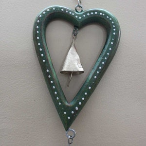 Puede incluir: Un carill&oacute;n de madera verde en forma de coraz&oacute;n con lunares blancos y una campana dorada en su interior. El carill&oacute;n est&aacute; encordado con cuentas de vidrio azules y marrones.