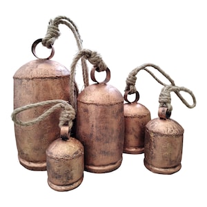 May include: A collection of five copper-colored metal bells of varying sizes. Each bell has a rustic, textured finish and is suspended by a natural rope. The bells are arranged together, suggesting a decorative or ornamental purpose.
