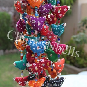 May include: A colorful beaded garland featuring fabric bird ornaments in various colors, including red, blue, yellow, and purple. Each bird is adorned with white polka dots and sequins. Gold bells hang at the bottom. The text "Chimes N bells" is visible.