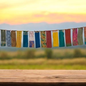 Könnte beinhalten: Ein Holztisch mit einem verschwommenen Hintergrund eines Feldes und einer Reihe bunter Stofffahnen, die an einem Sonnenuntergangshimmel in der Luft hängen.