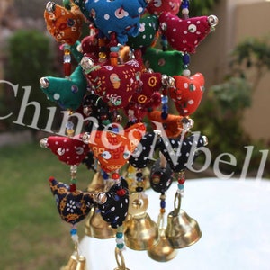 May include: A colorful hanging decoration featuring fabric bird shapes in various colors and patterns, strung together with beads. Each bird has a small bell attached. The word "Chimes" is partially visible.