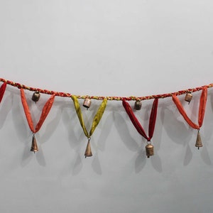 Puede incluir: Una guirnalda de campanas con acentos de tela roja, naranja y amarilla. La guirnalda está hecha de una cuerda trenzada y tiene un total de 10 campanas. El texto "By ChimesNbells" es visible en la esquina inferior derecha de la imagen.