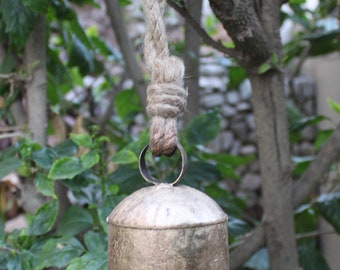 May include: A rustic, silver-toned bell with a rope hanging from it. The bell is hanging from a tree branch.