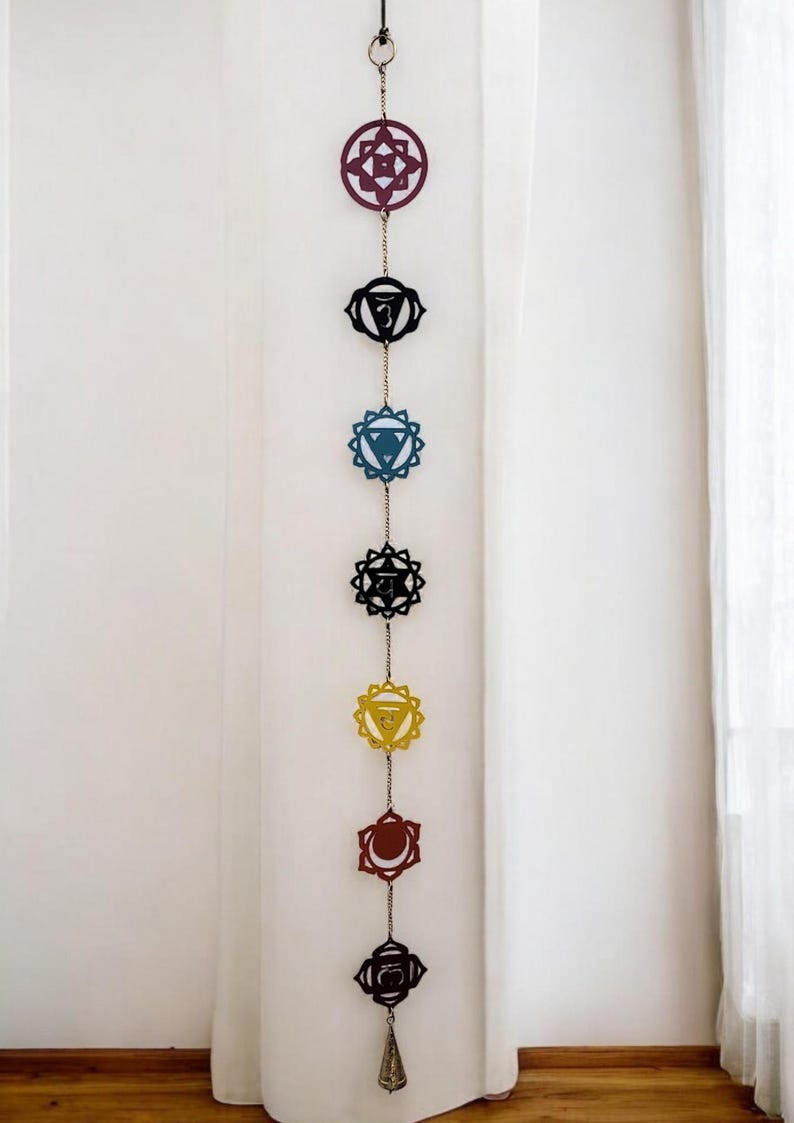 Pu&ograve; includere: Un arazzo da parete a sette chakra con una campana in fondo. I chakra sono rappresentati da simboli colorati, tra cui rosso, arancione, giallo, verde, blu, indaco e viola.