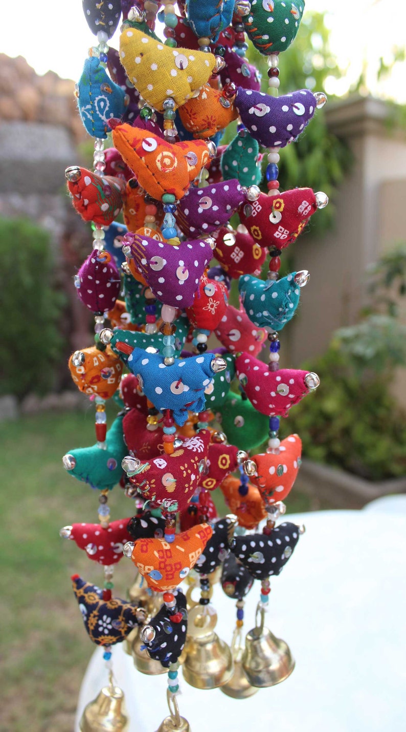 May include: A colorful garland of fabric birds in various colors, including red, blue, and yellow, adorned with white polka dots and sequins. The birds hang from beaded strands, with small bells at the bottom. A decorative item.