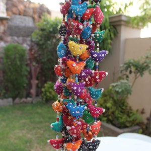 May include: A colorful beaded hanging decoration featuring fabric bird shapes in various colors like red, blue, and yellow. The birds are adorned with white polka dots and small bells hang at the bottom. The background is blurred.