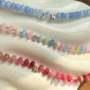 Peut inclure: Trois colliers de perles avec des perles de différentes couleurs. Le collier supérieur a des perles bleu clair avec les lettres "J" et "N". Le collier du milieu a des perles roses, bleues et jaunes avec la lettre "E". Le collier inférieur a des perles rouges et roses avec la lettre "A".
