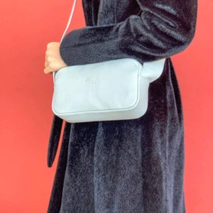 K&ouml;nnte beinhalten: Eine hellgraue Leder-Umh&auml;ngetasche mit einem Riemen und einem Logo mit der Aufschrift "Leaves & Co."